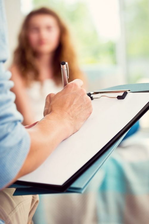 Teenager girl visiting a psychologist. Close up of human hand and clipboard.